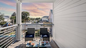 Ein Balkon mit Korbmöbeln, einem Glastisch und Blick auf die Nachbarschaft.