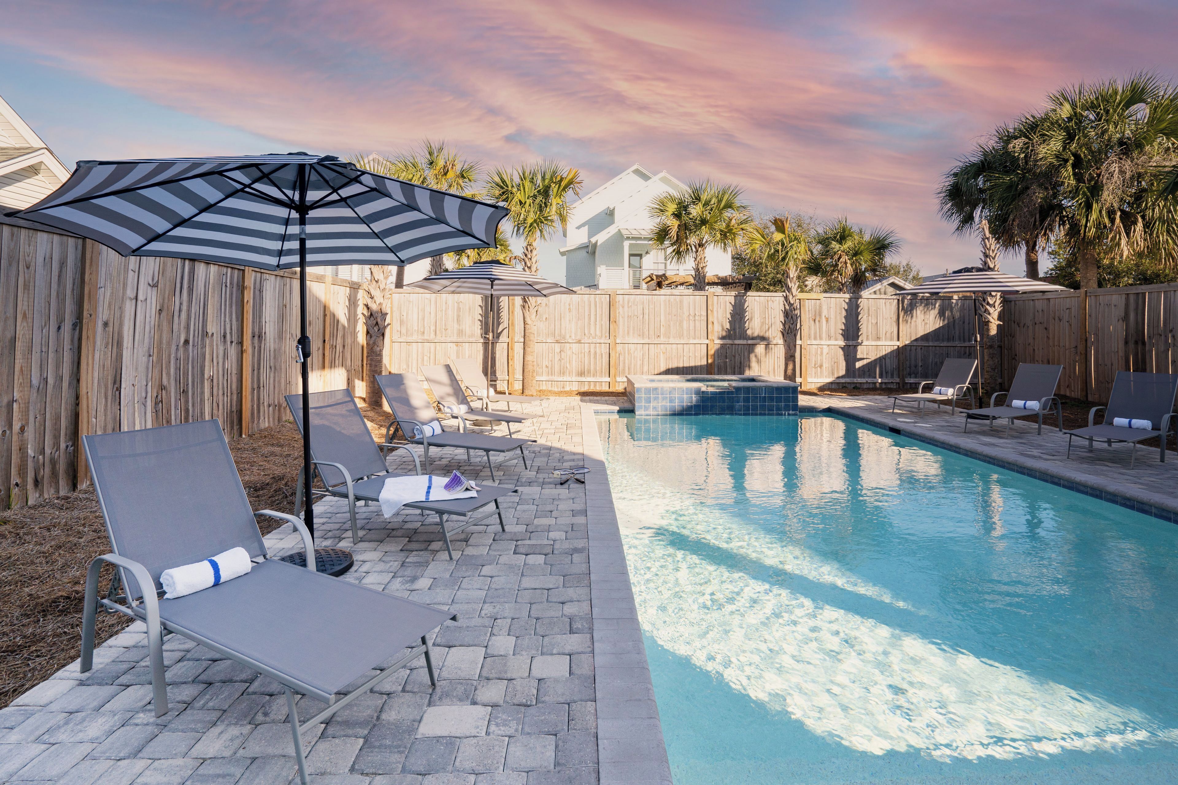 A backyard with a swimming pool, lounge chairs, and a wooden fence.