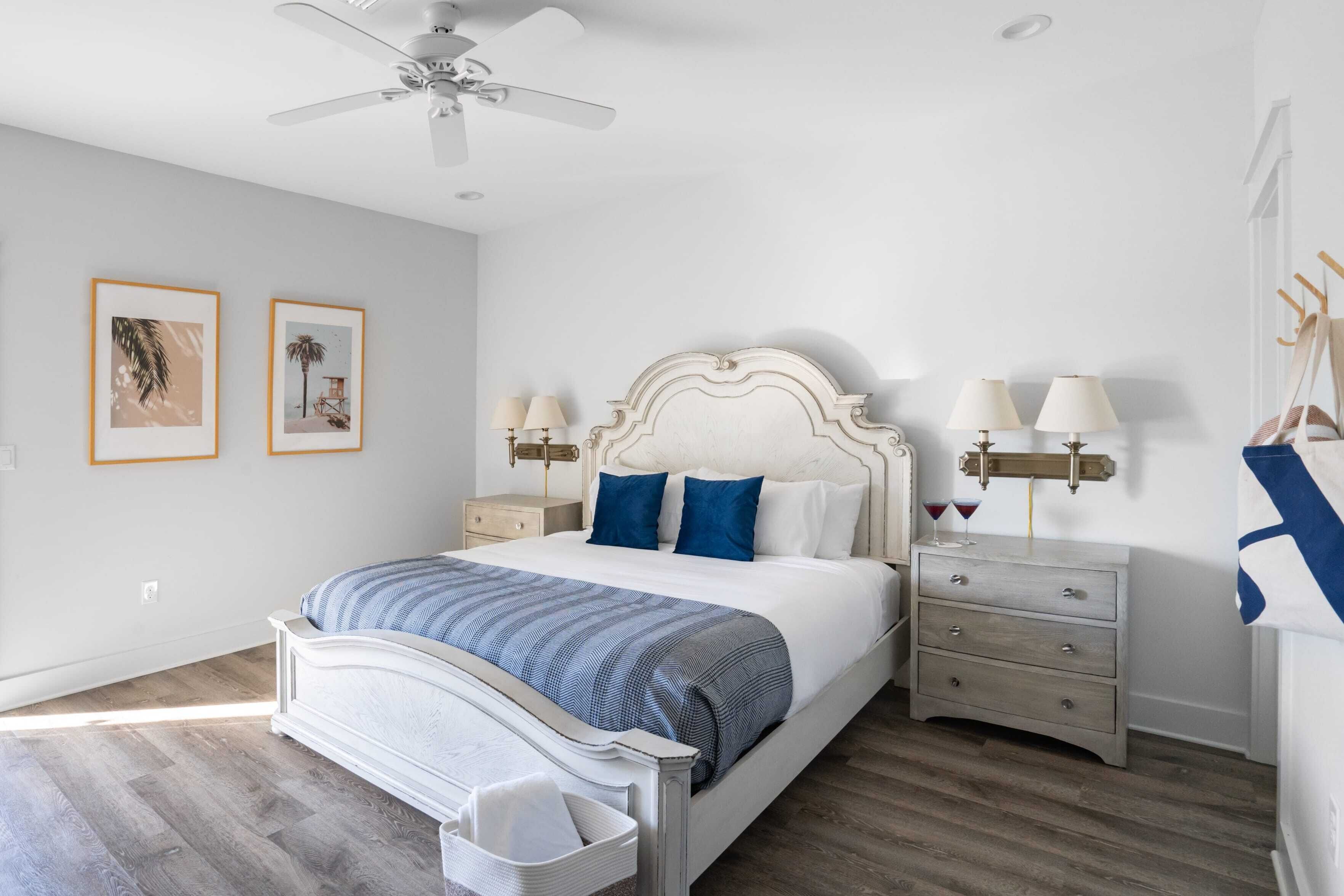 A bedroom with a bed, nightstands, a ceiling fan, and wall-mounted lamps.