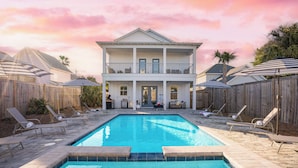 Ein zweistöckiges Haus mit Swimmingpool, Liegestühlen und Sonnenschirmen.