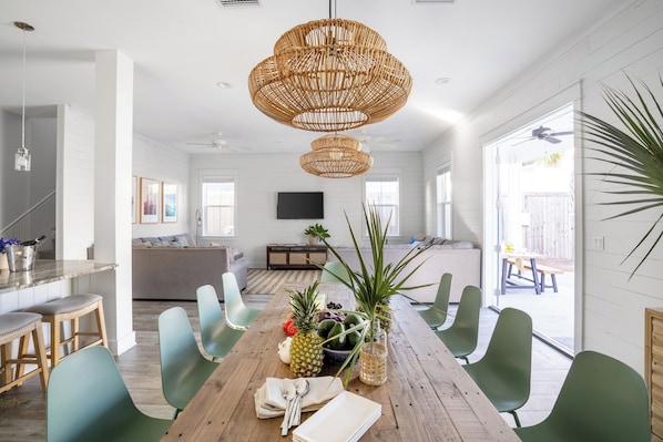 Un comedor espacioso con una mesa de madera, sillas verdes y una lámpara trenzada grande.