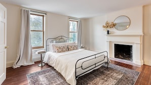 Une chambre à coucher avec un lit, deux fenêtres, une cheminée et un miroir.