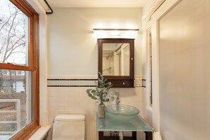A bathroom with a glass sink, a white toilet, a mirror, and a window. - Elliot by Avantstay Historic Character Home in Great Location! (Saugerties)