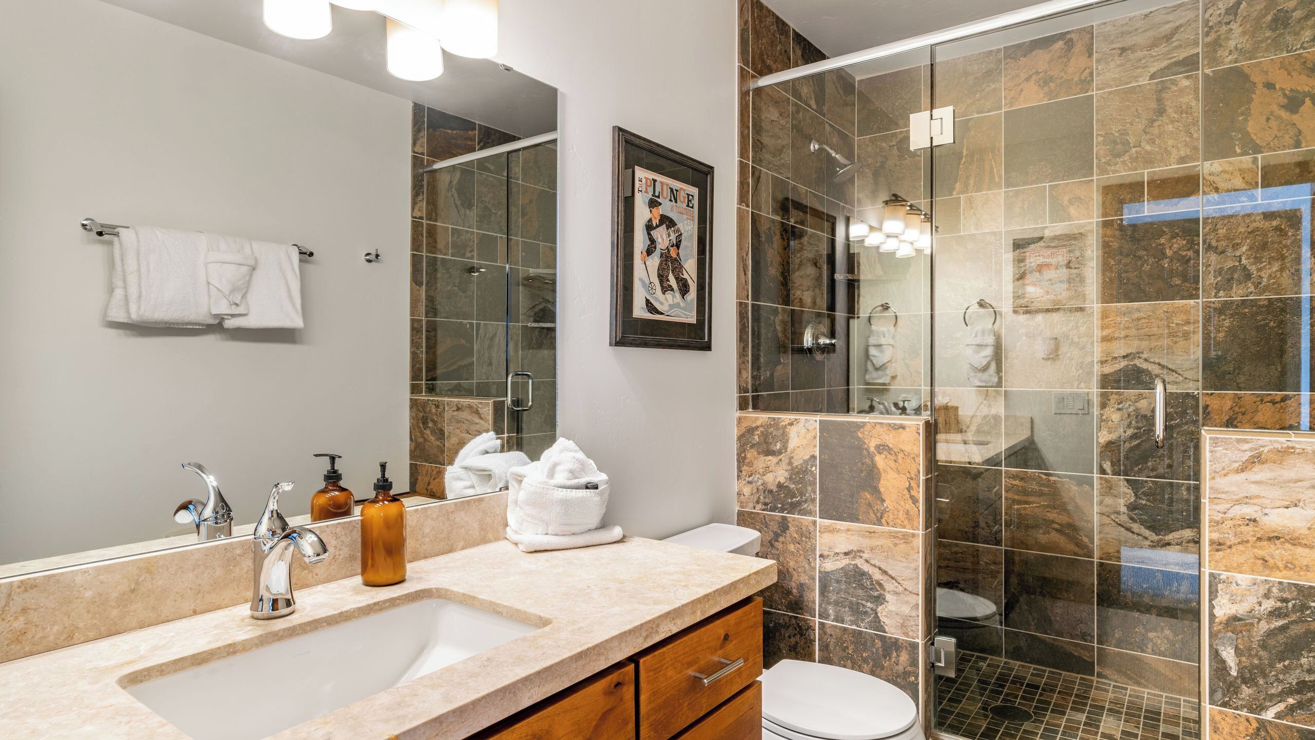 A modern bathroom with a large sink, two mirrors, a shower enclosure, and a framed picture on the wall.