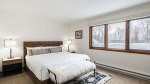 A bedroom with a wooden headboard, a large bed, two bedside tables with lamps, a window with a view of a snowy landscape, and a rug. - Riverside Condos C202 by Avantstay Condo Close To Downtown, Town Park & Ski Lift #8 (Telluride)