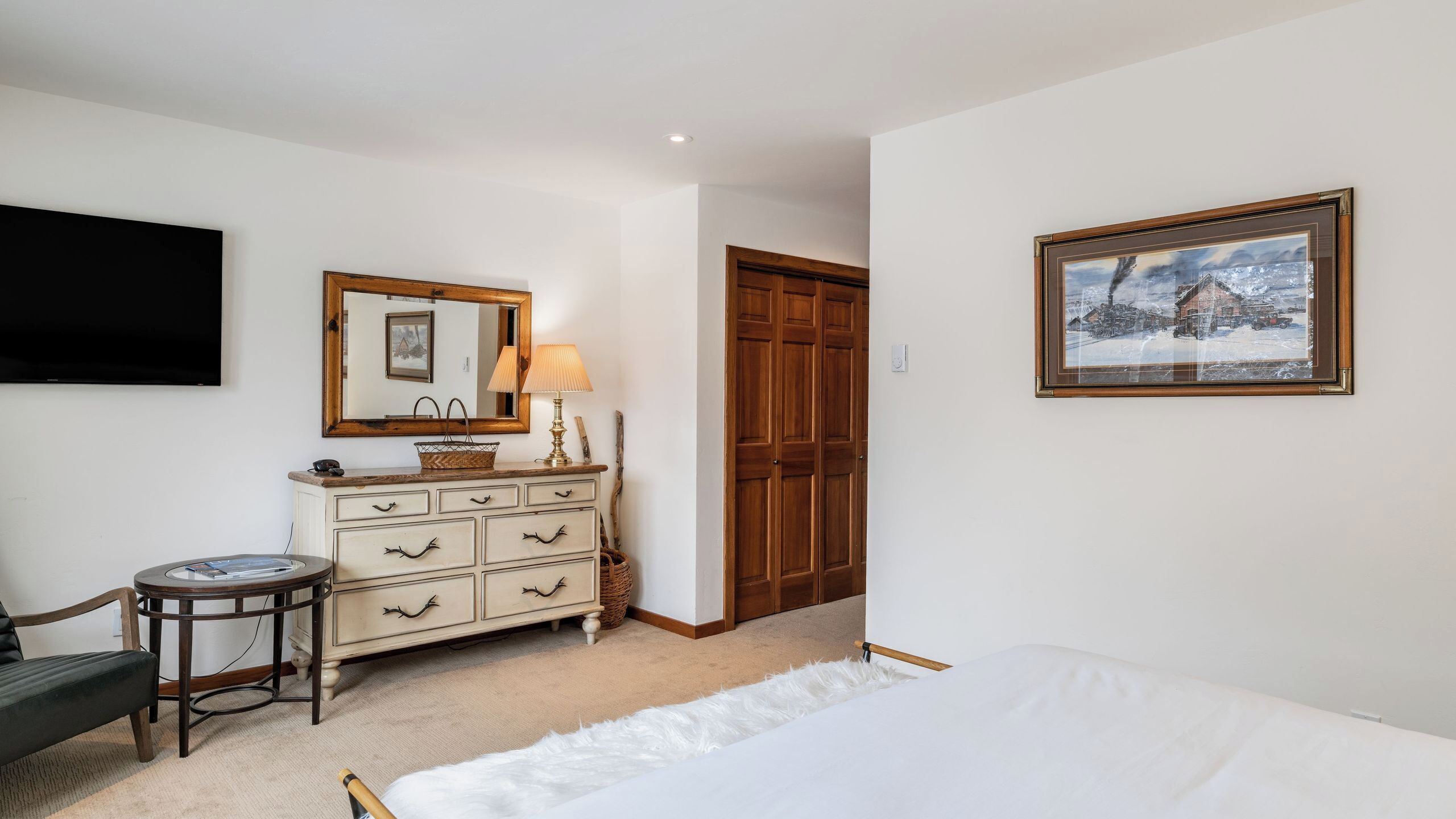 Une chambre à coucher avec un lit, une commode, un miroir, une lampe et un tableau.