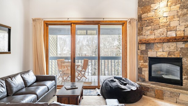 A living room with a leather sofa, a wooden coffee table, a black bean bag, and a stone fireplace. - Riverside Condos C202 by Avantstay Condo Close To Downtown, Town Park & Ski Lift #8 (Telluride)