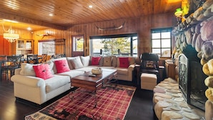 A cozy cabin interior with a wooden ceiling, stone fireplace, and a dining area with a view of the outdoors. - Shoreline Lakehouse by Avantstay Majestic Lakefront Cabin w/ Hot Tub & Fire Pit! (Big Bear Lake)