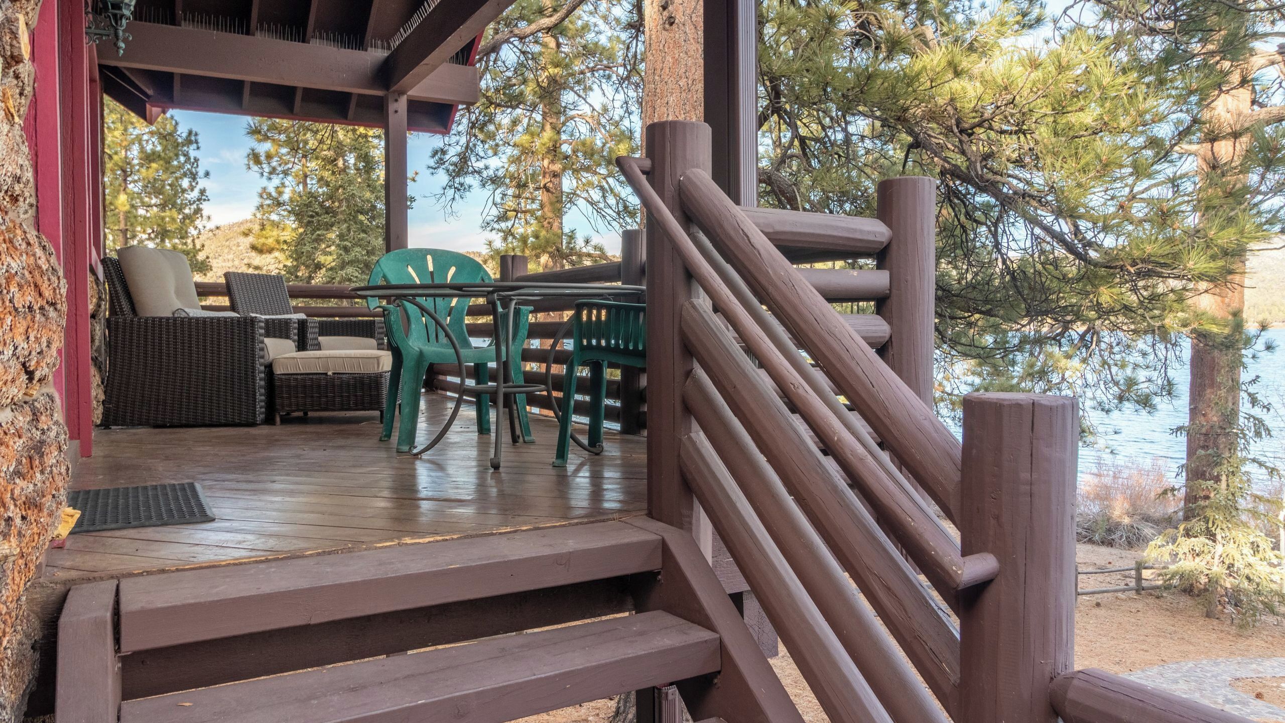 A wooden deck with outdoor furniture, a staircase, and a view of trees and water.