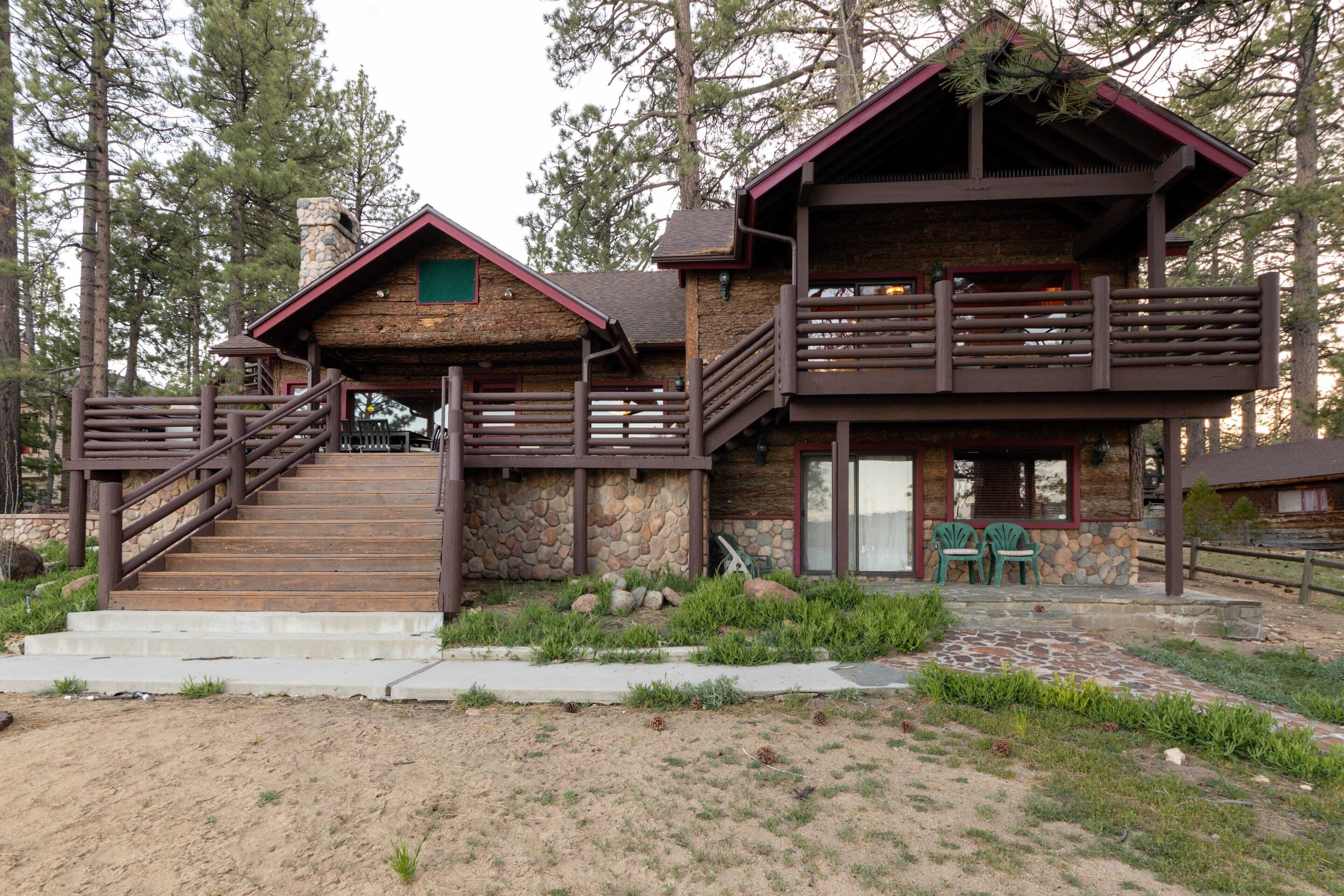 A rustic cabin with a stone facade, wooden deck, and a staircase leading to a balcony.