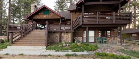 A rustic cabin with a stone facade, wooden deck, and a staircase leading to a balcony.