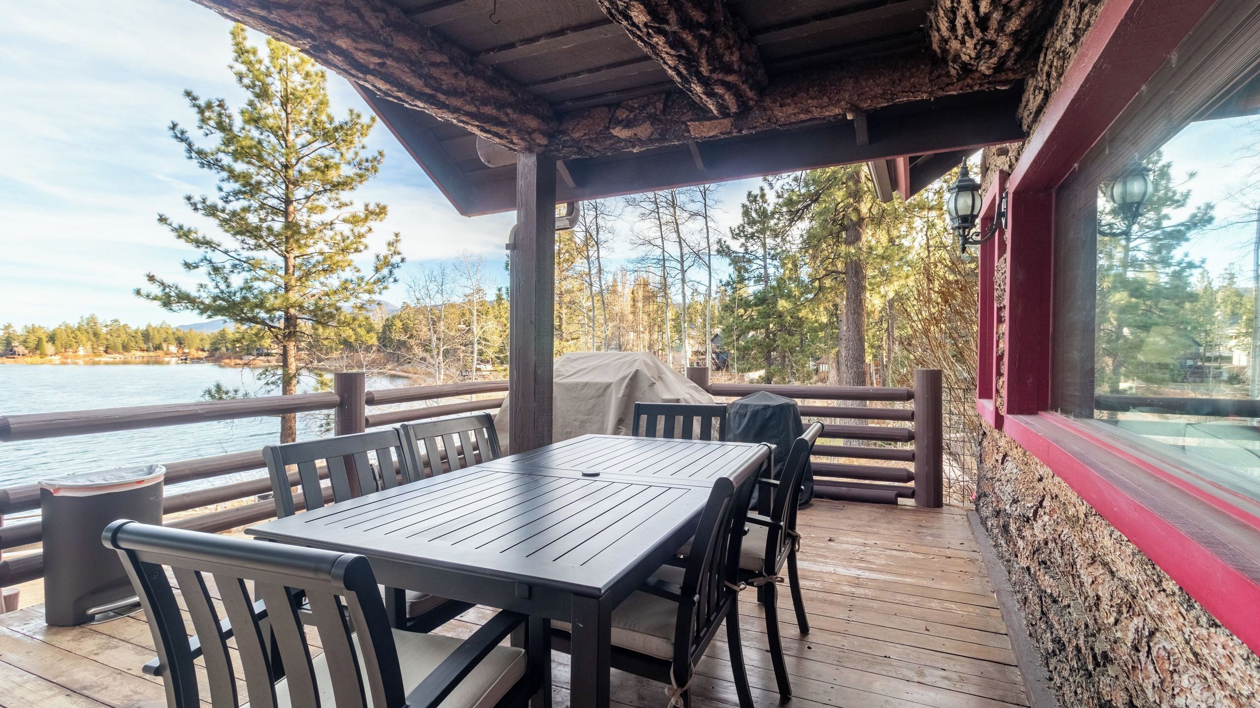 An outdoor deck with a table and chairs, overlooking a body of water and surrounded by trees.