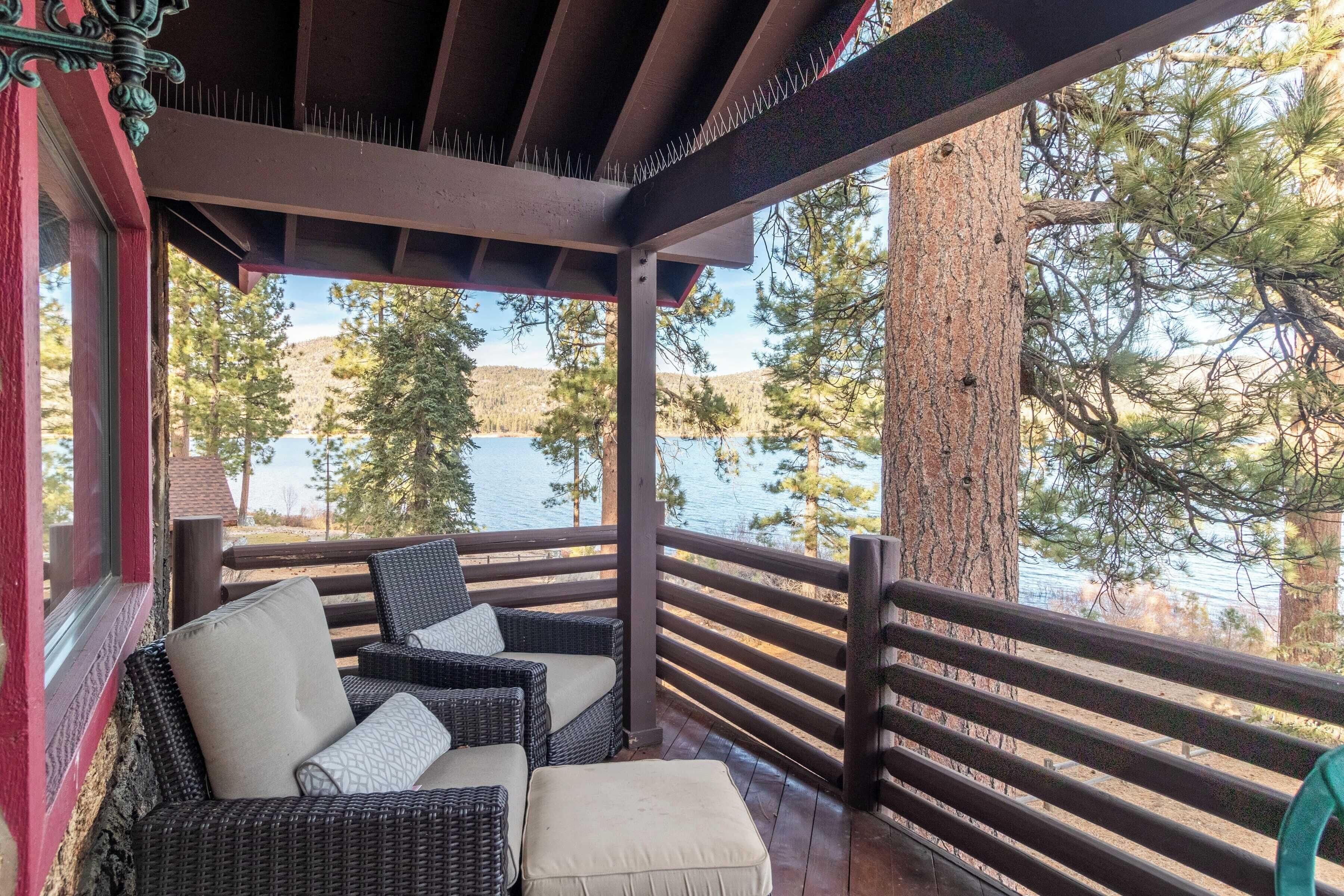 A covered outdoor seating area with wicker furniture and a view of a lake and trees.