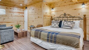 Ein gemütliches Holzblockhaus-Zimmer mit einem Bett, einem grauen Sofa, einem kleinen Tisch mit Pflanze und einem Nachttisch.