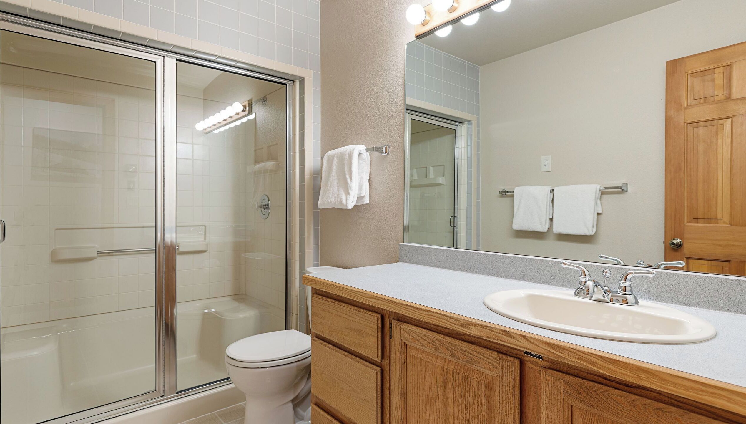 A bathroom with a glass shower enclosure, a toilet, a sink with a mirror, and wooden cabinets.