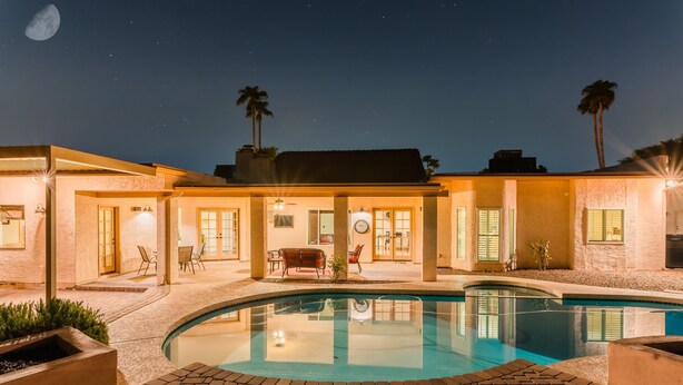 A poolside area with a clear pool, a patio with chairs, and a building with a moon in the background. - Desert Ridge by Avantstay Spacious Oasis w/ Pool & Hot Tub (Scottsdale)