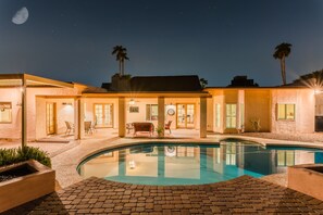A poolside area with a clear pool, a patio with chairs, and a building with a moon in the background. - Desert Ridge by Avantstay Spacious Oasis w/ Pool & Hot Tub (Scottsdale)