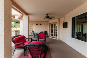 Ein überdachter Patio-Bereich mit Korbmöbeln, einem Deckenventilator und einem an der Wand befestigten Fernseher.