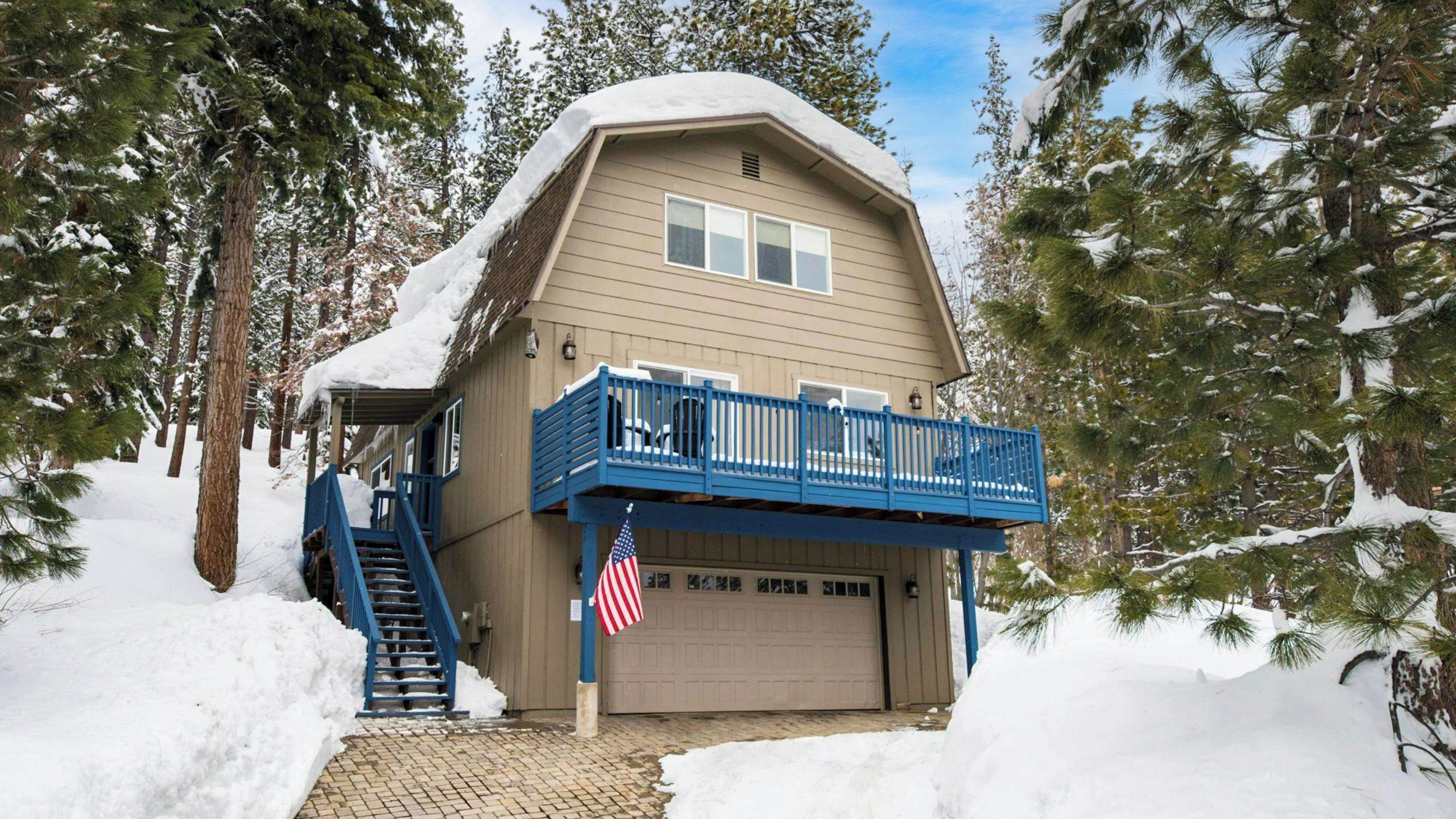Una casa de dos pisos con un garaje, rodeada de árboles cubiertos de nieve.