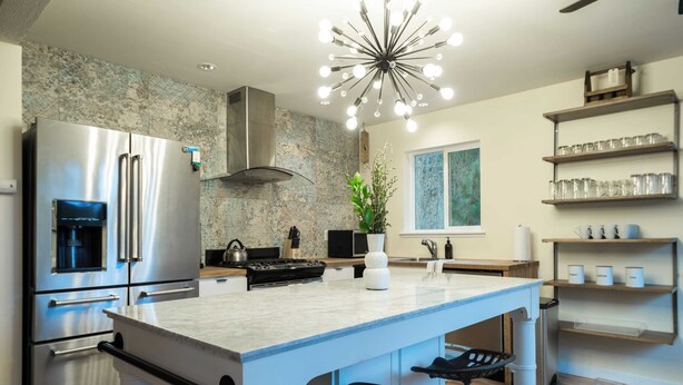 A modern kitchen with a large island, stainless steel appliances, and a unique ceiling light fixture.