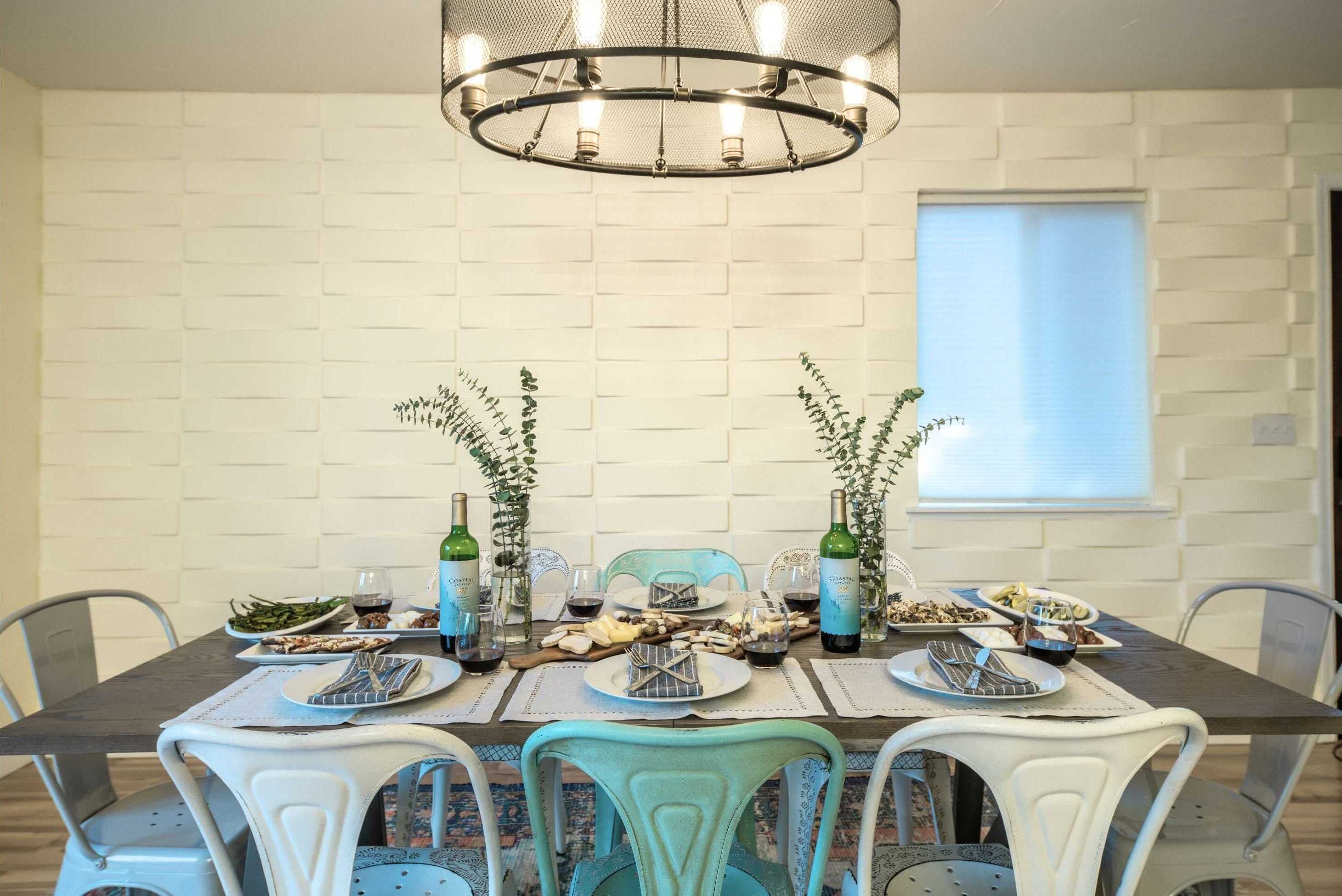 A dining table set with plates, cutlery, and glasses, surrounded by chairs with a white and teal color scheme, under a modern chandelier.