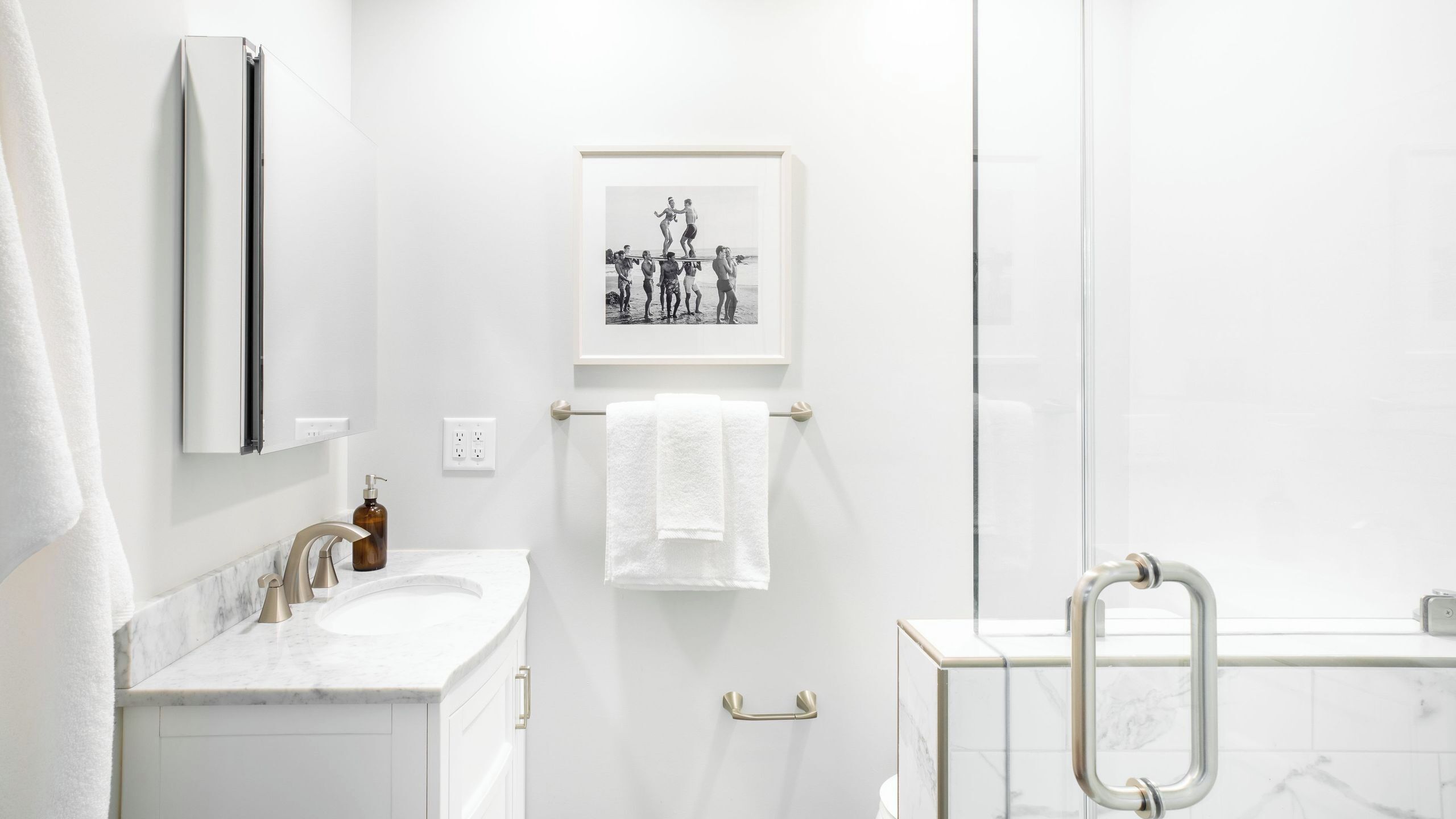 Ein modernes Badezimmer mit einem Marmorwaschbecken, einem in Rahmen befindlichen Schwarz-Weiß-Foto und einer Duschkabine aus Glas.