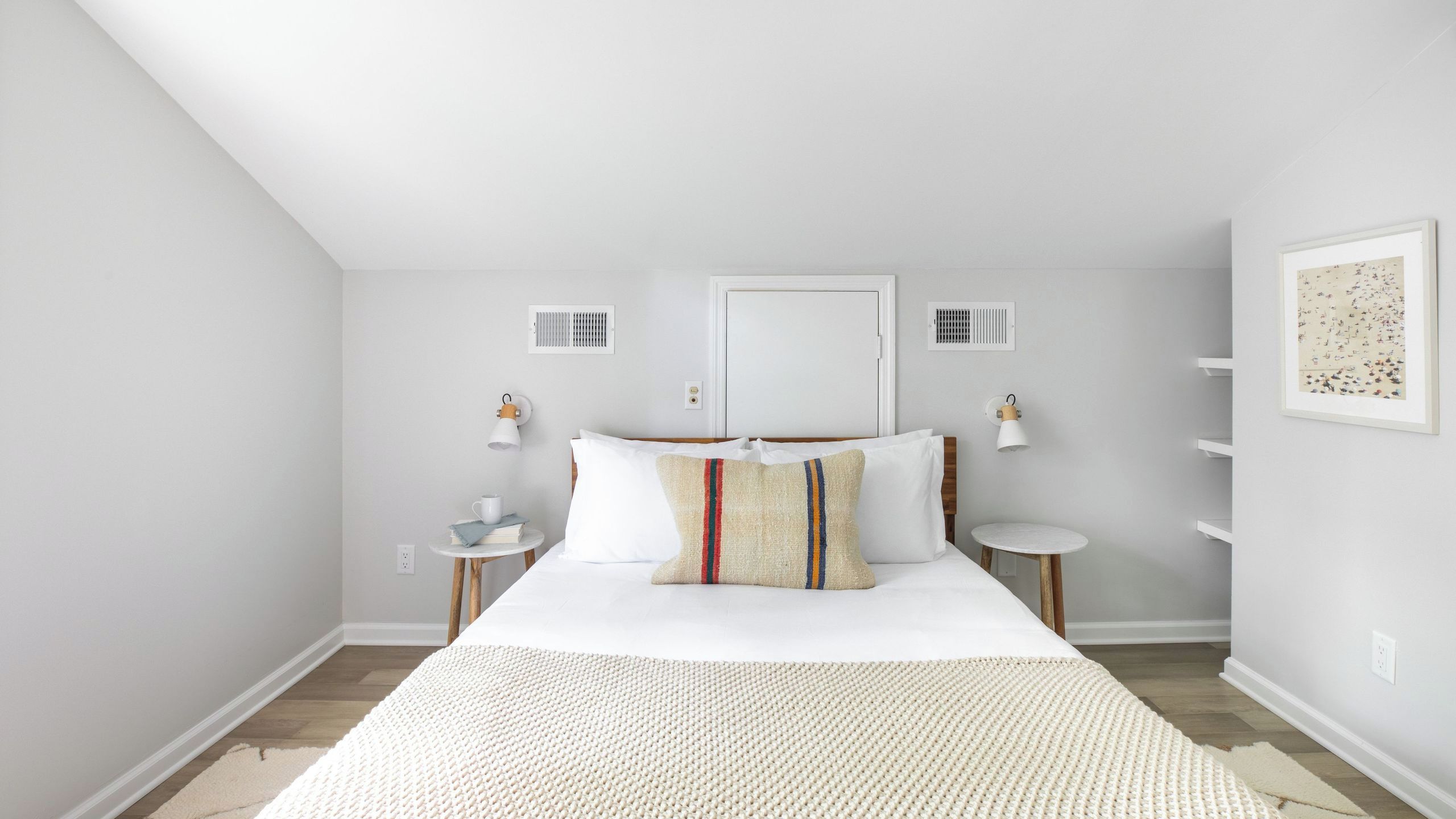 A bedroom with a bed, bedside tables, a round table, a door, and a wall-mounted shelf.