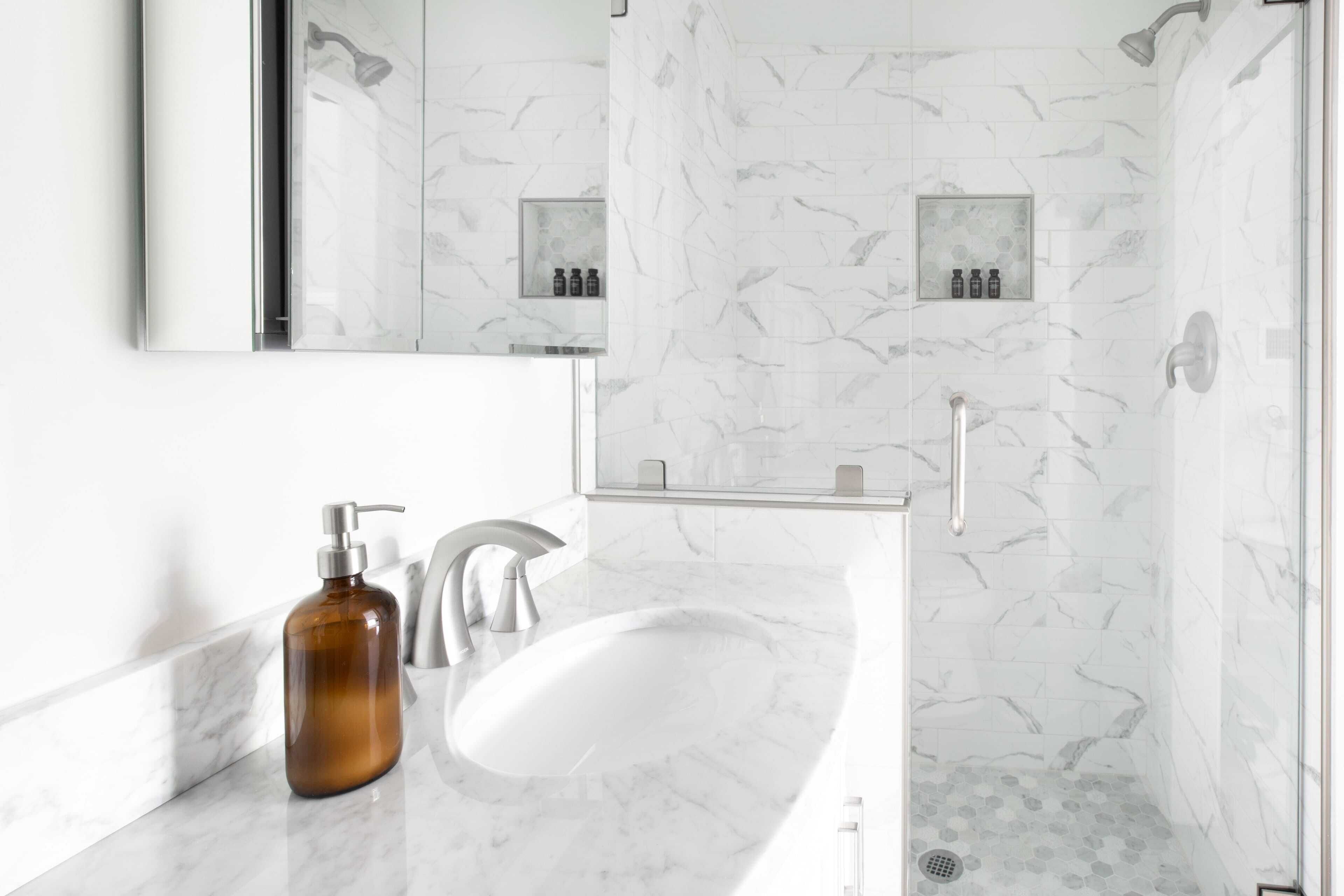 A modern bathroom with a marble sink, a shower with a glass door, and a mirror above the sink.