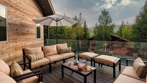 Una terraza de madera con un sofá, sillas y una sombrilla.