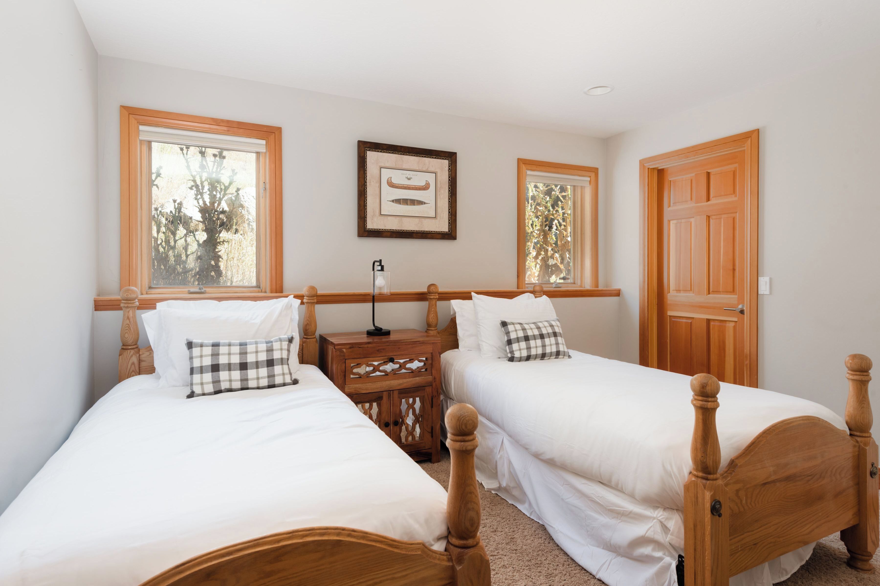 A bedroom with two beds, a nightstand, a framed picture, and a wooden door.