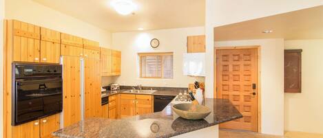 A kitchen with wooden cabinets, a granite countertop, a built-in oven, a sink, and a clock on the wall.