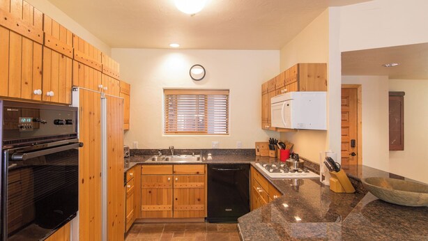 A kitchen with wooden cabinets, a built-in oven, a microwave, a sink, and a window with blinds. - Westermere 311 - 2 by Avantstay Just Steps From Ski Area w/ Great Views! (Telluride)