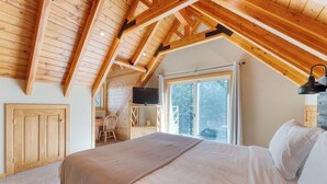 Un dormitorio con techo de madera, una cama, un escritorio y una silla.