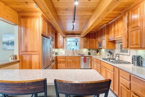 A kitchen with wooden cabinets, granite countertops, stainless steel appliances, and a window with a view of trees. - Ember by Avantstay Majestic Entertainers Home w/ Pine Tree Views & Close to Meek's Bay (Tahoma)
