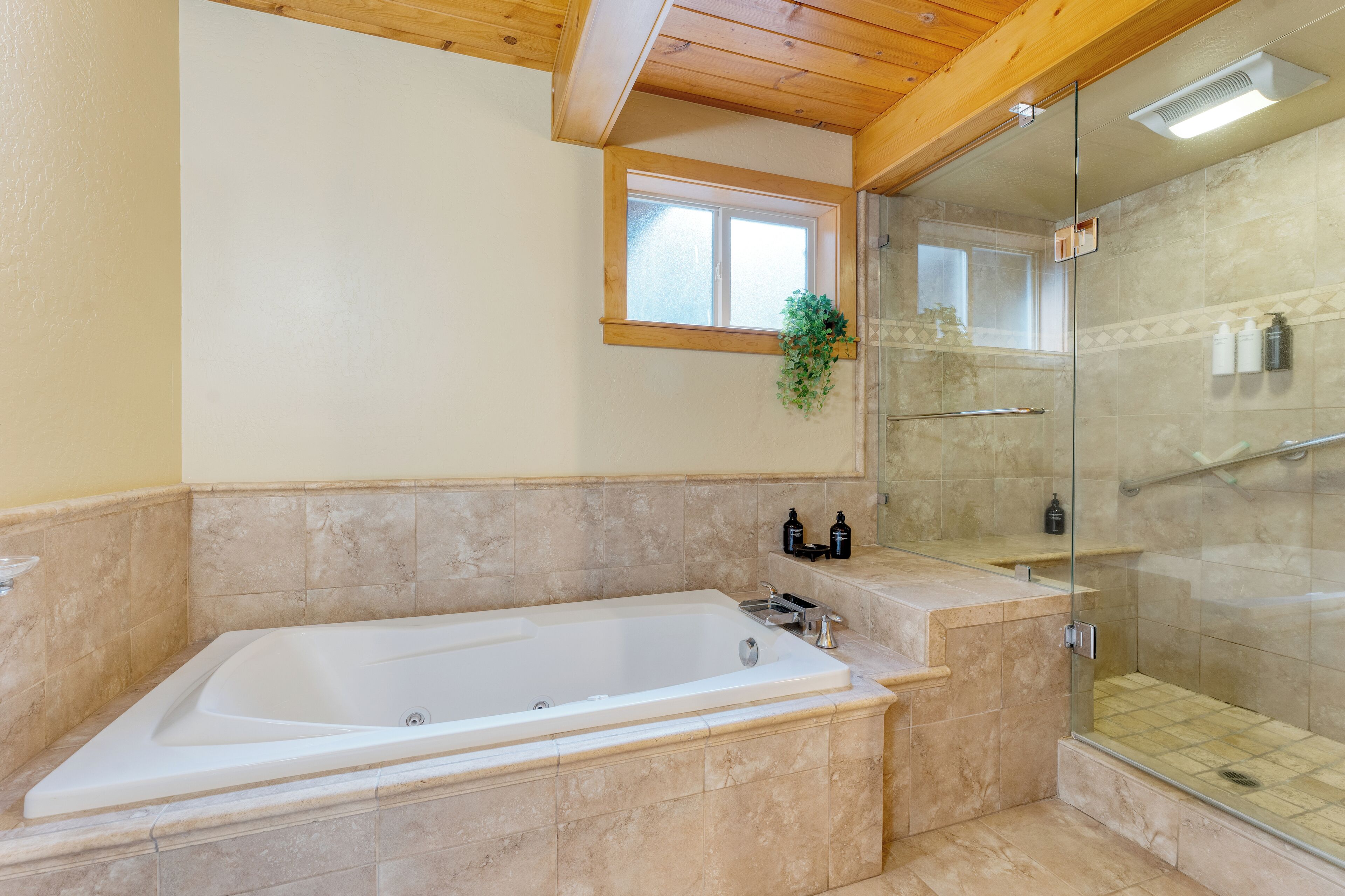 A bathroom with a large bathtub, a glass-enclosed shower, and a window above the bathtub.