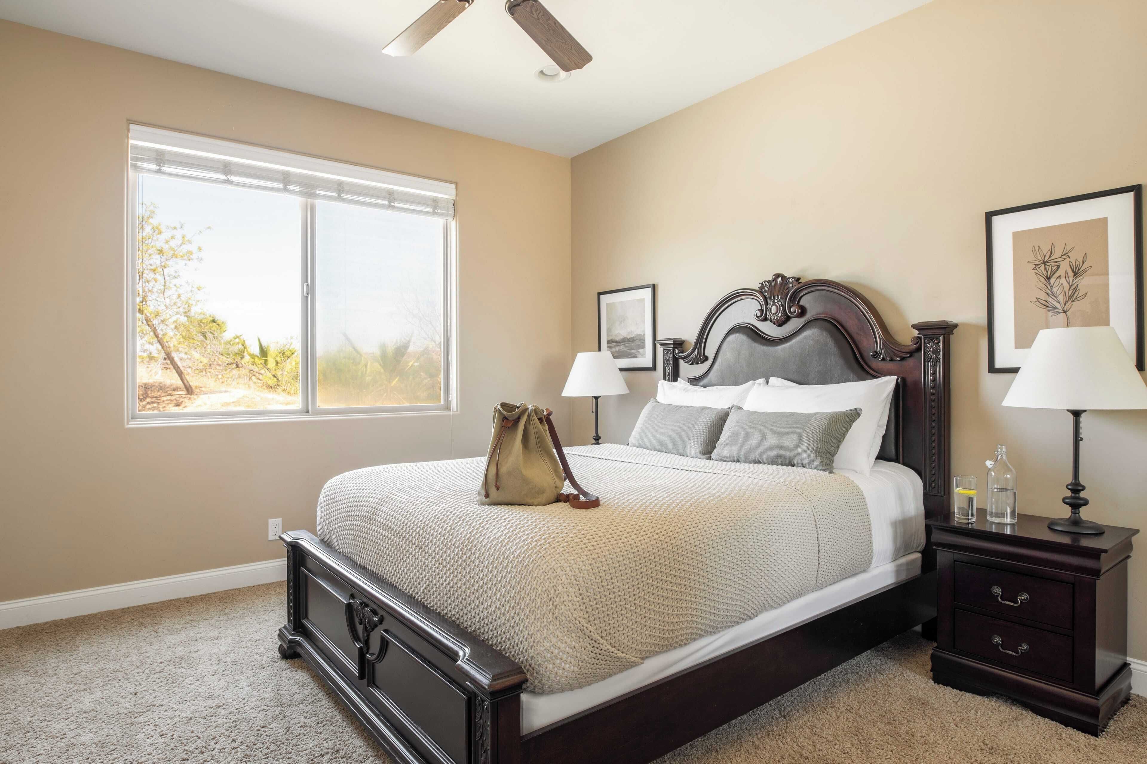 A bedroom with a large bed, a nightstand, a window with blinds, and a ceiling fan.