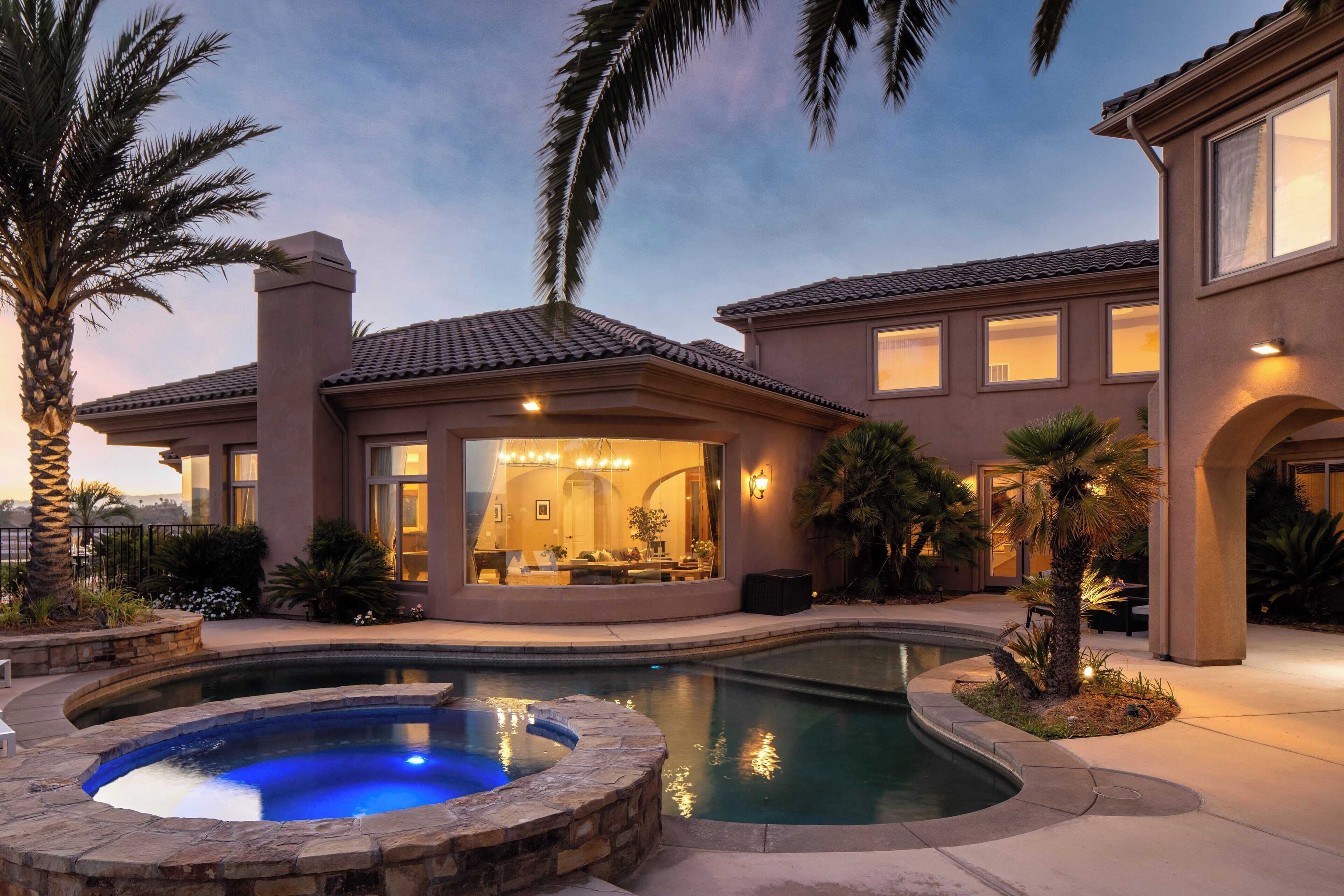 A residential property with a swimming pool, a hot tub, and a well-lit interior.