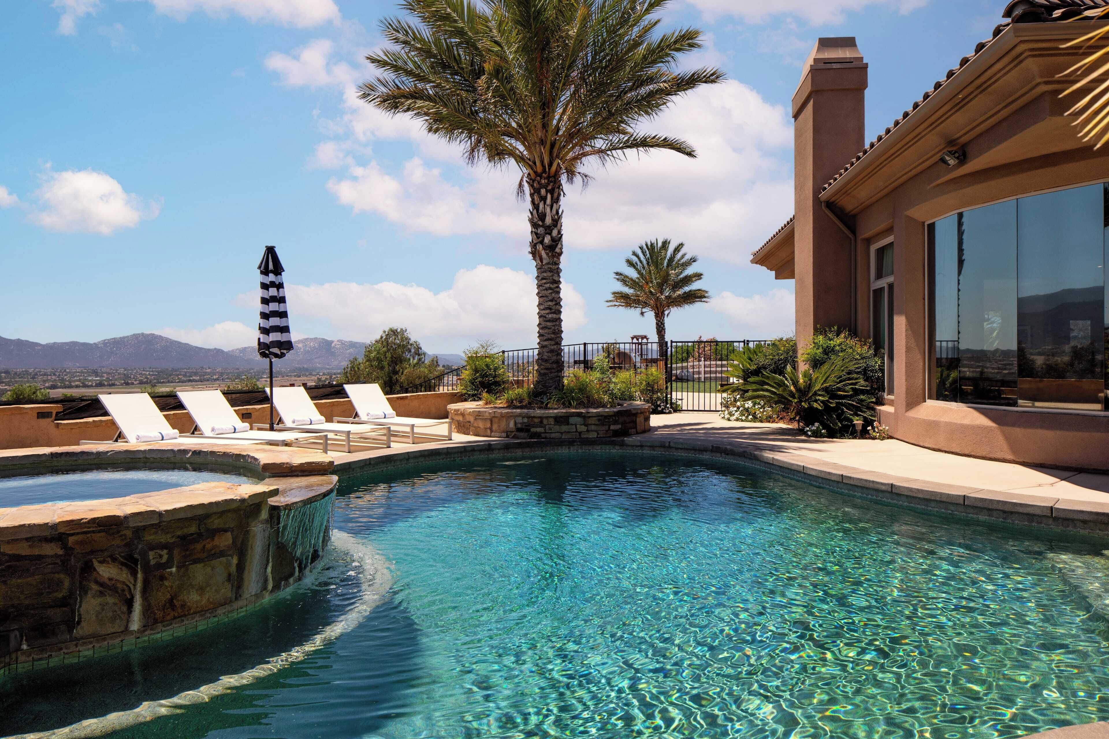 A swimming pool with lounge chairs, palm trees, and a mountain view.