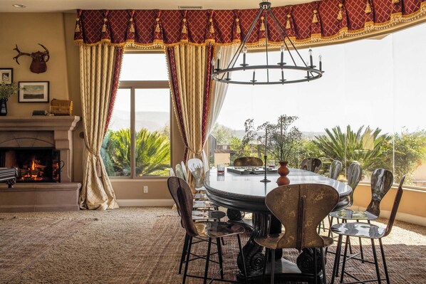 A dining area with a round table, chairs, a chandelier, and a fireplace.