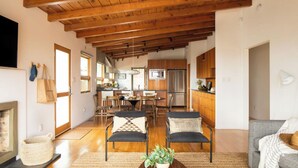 Amplia sala de estar con chimenea, vigas de madera en el techo, una mesa de comedor con sillas y una cocina al fondo.