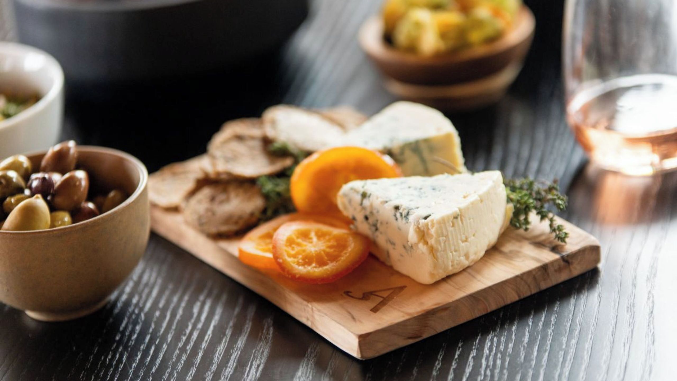 Une planche en bois garnie de fromage, d’olives et d’une tranche de tomate.