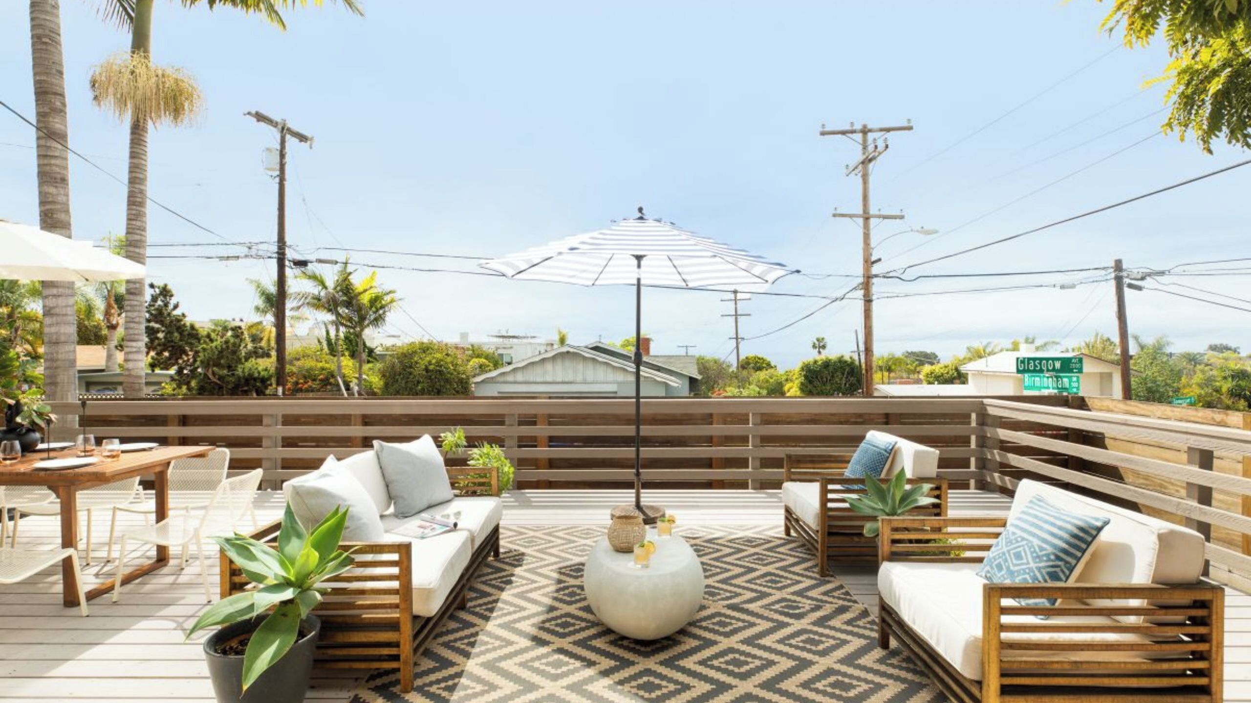 Eine Terrasse mit Gartenmöbeln, einem gemusterten Teppich und einem großen Sonnenschirm.