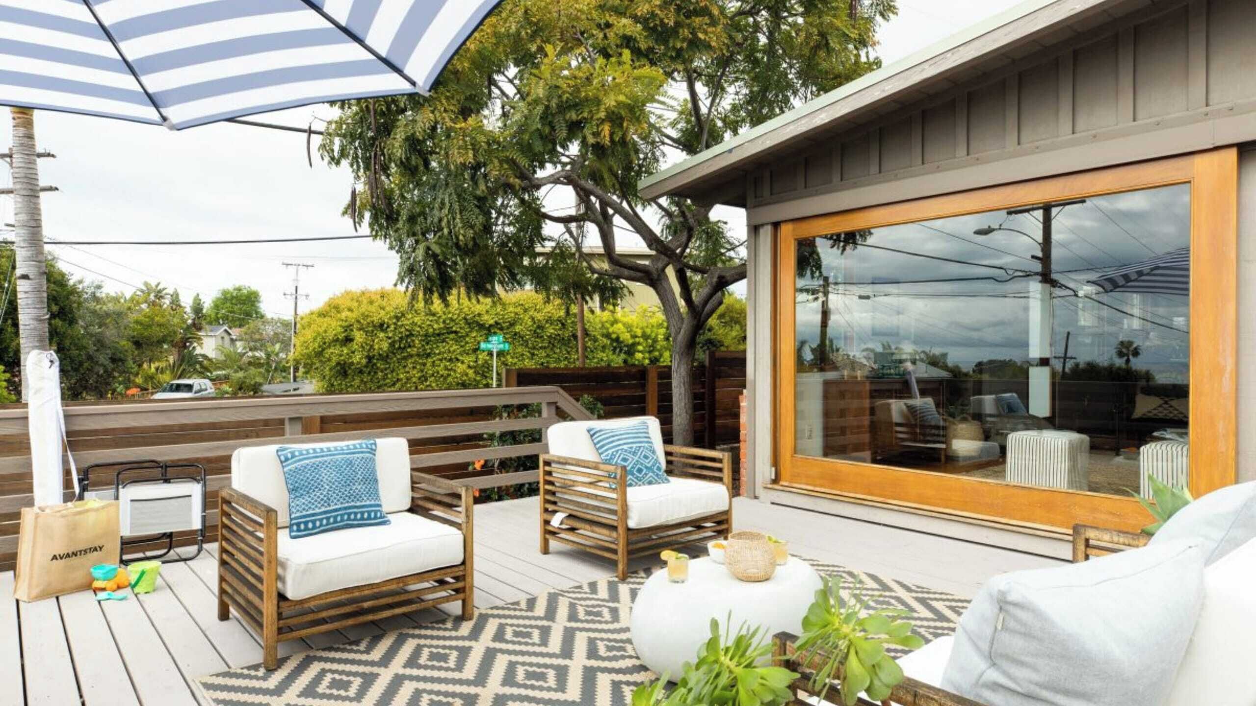 Une terrasse extérieure avec des meubles en bois, un parasol à rayures et une grande porte-fenêtre coulissante.