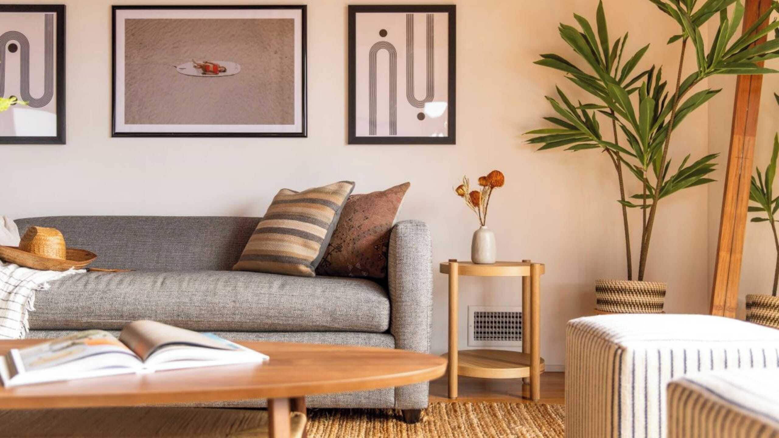 A living room with a grey sofa, a wooden coffee table, a small side table with a vase, and a large plant.