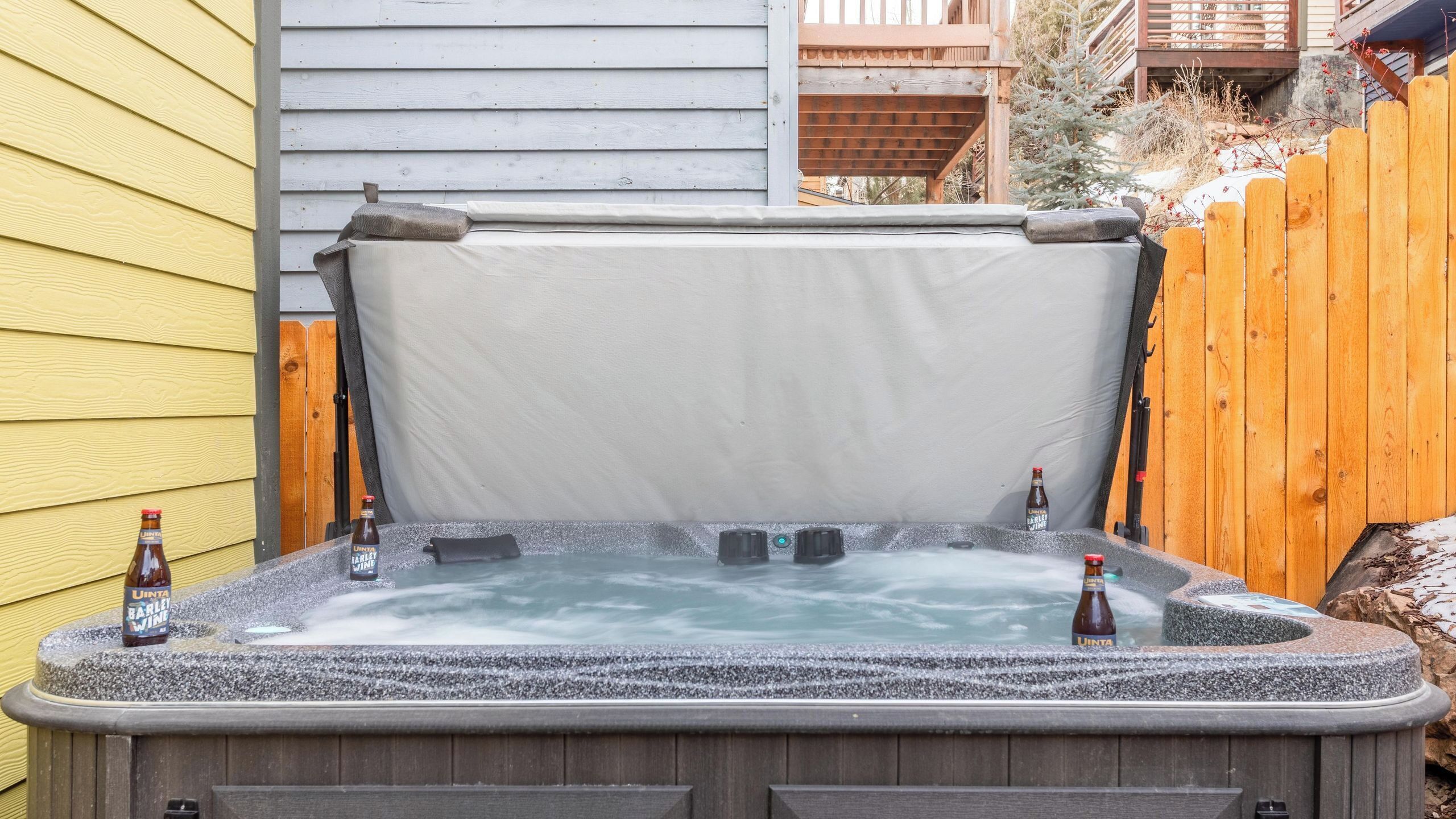 Un jacuzzi con tapa, dos botellas de cerveza y una cerca de madera al fondo.