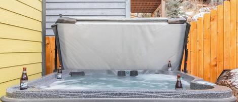 Un jacuzzi con tapa, dos botellas de cerveza y una cerca de madera al fondo.