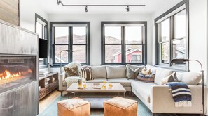 A modern living room with a fireplace, large windows, a sofa, and a coffee table.