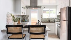 A modern kitchen with white cabinets, a stainless steel refrigerator, a gas stove, and two wicker chairs. - Hamilton II by Avantstay Beach House Rooftop Deck Newly Renovated Bungalow (La Jolla)