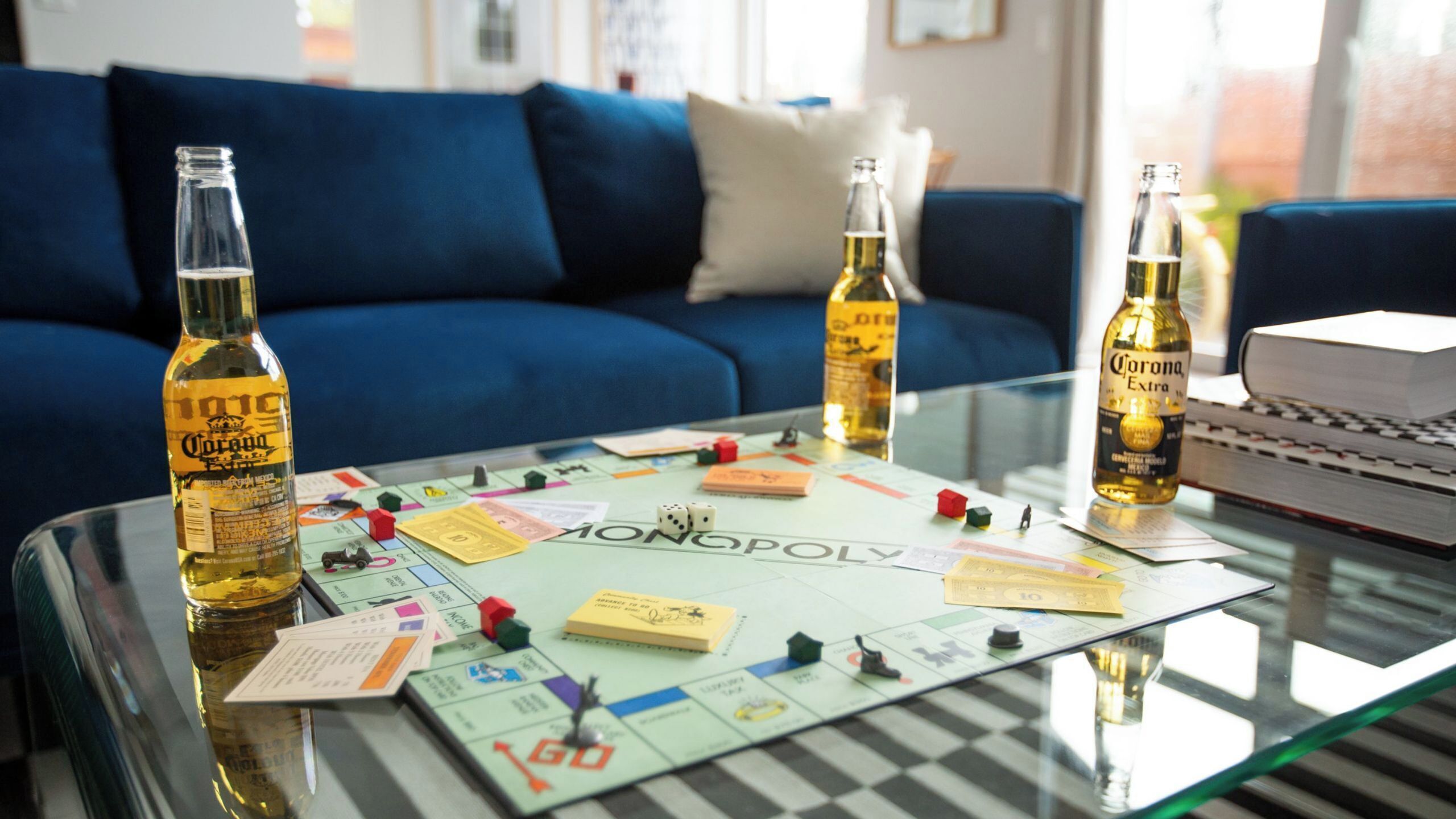 A Monopoly game on a glass table with three Corona beer bottles.