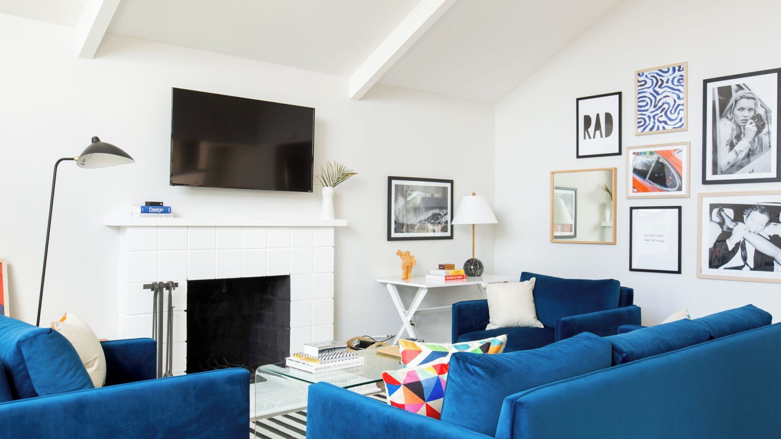 A modern living room with a fireplace, blue sofas, a flat-screen TV, and various framed pictures on the wall.